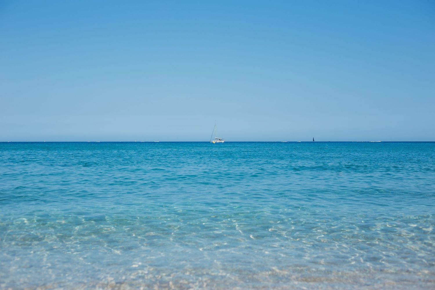 open blue sea with small white boat on the horizon