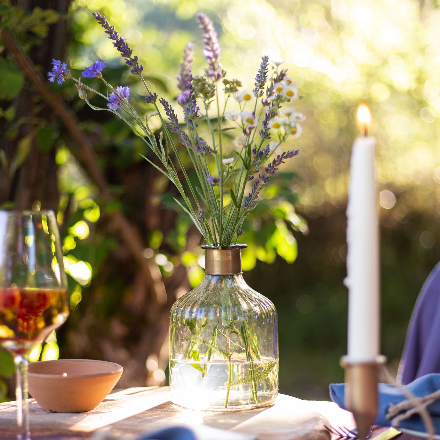 vase of lavender on table next to candlestick and glass of wine on table in garden at golden hour