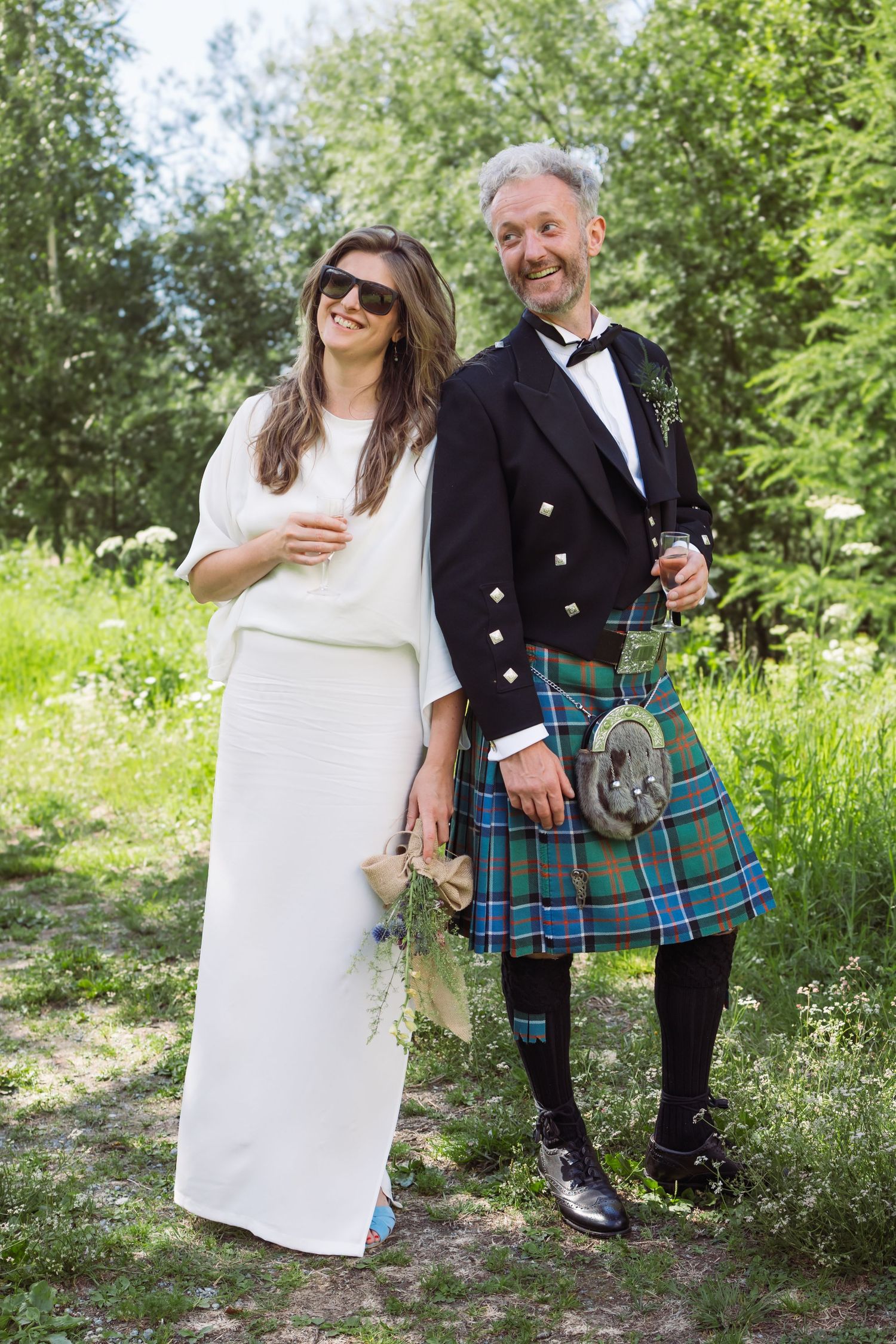 bride stands with sunglasses and champagne glass next to groom looking very cool