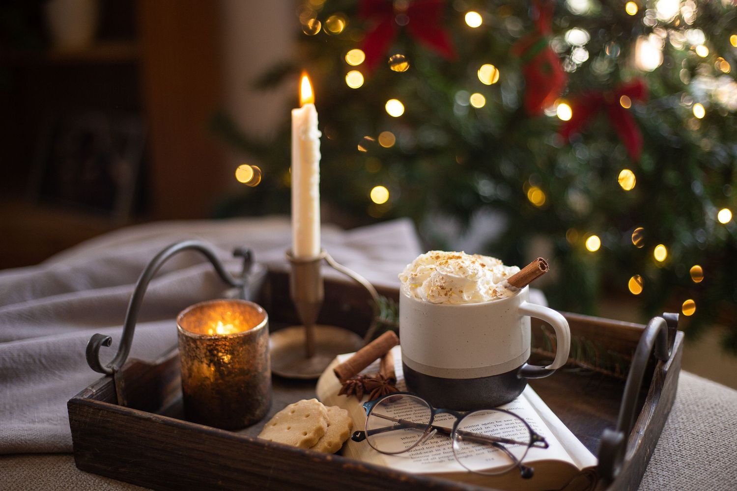 wooden serving tray with candles and mug of hot chocolate in front of Christmas tree
