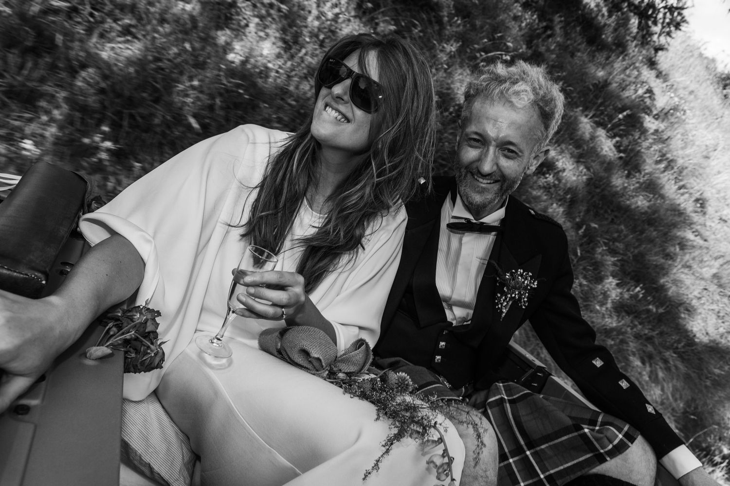 bride and groom ride in back of open top landcover holding champagne glass