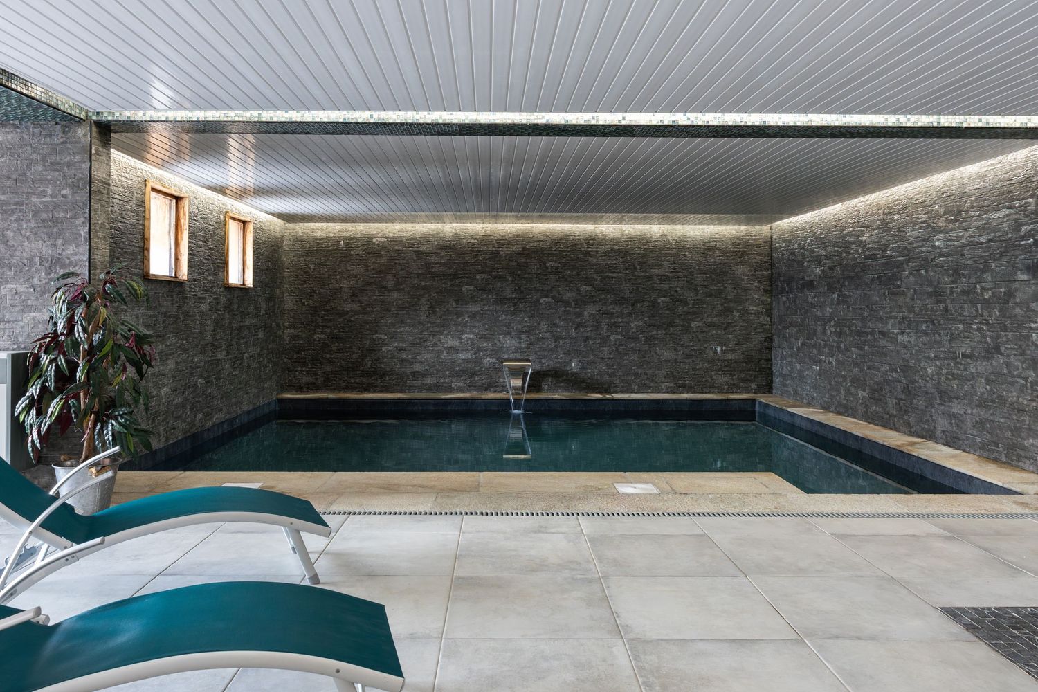 indoor swimming pool with two green loungers and plants