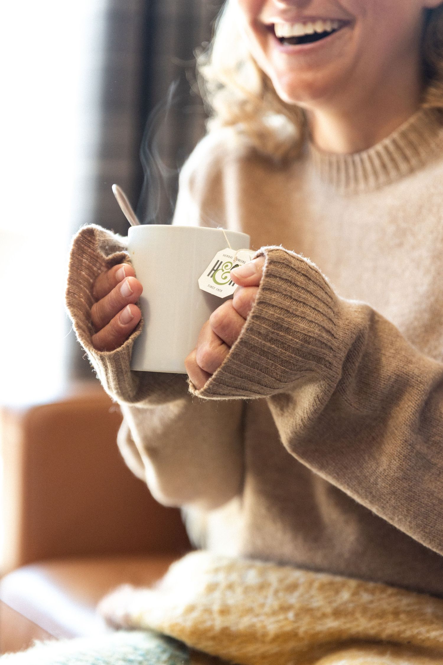 laughing lady hands tea mug close to chest as steam rises from mug