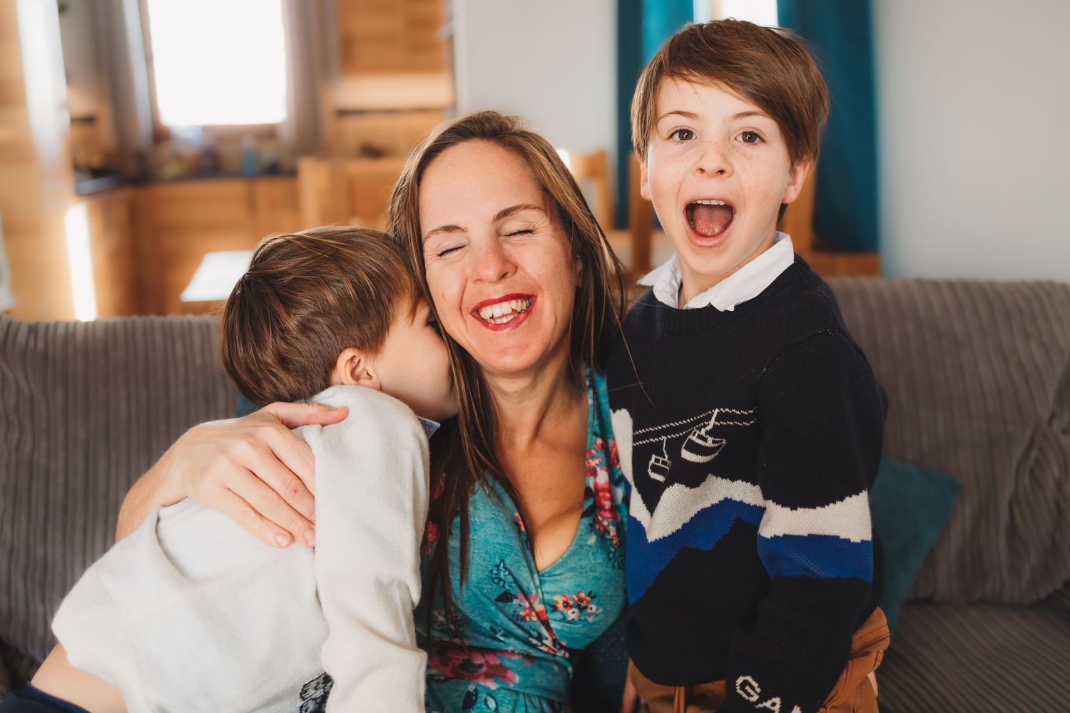 mother cuddles with two sons on sofa in ski apartment