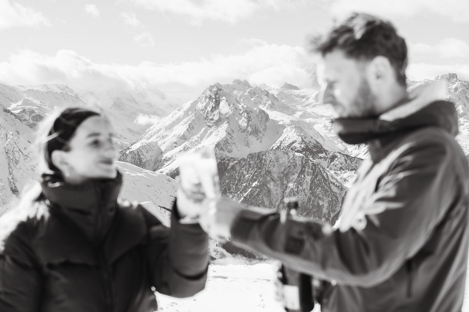 Couple shares glass of champagne on top of mountain after proposal