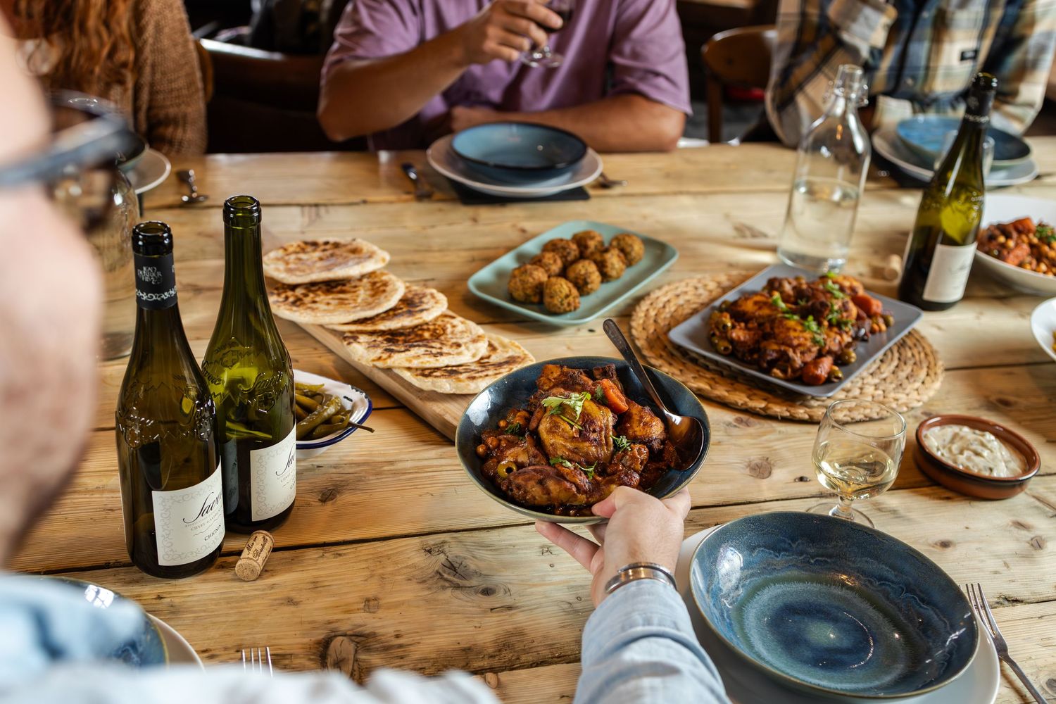 hand passes bowl of curry across wooden table