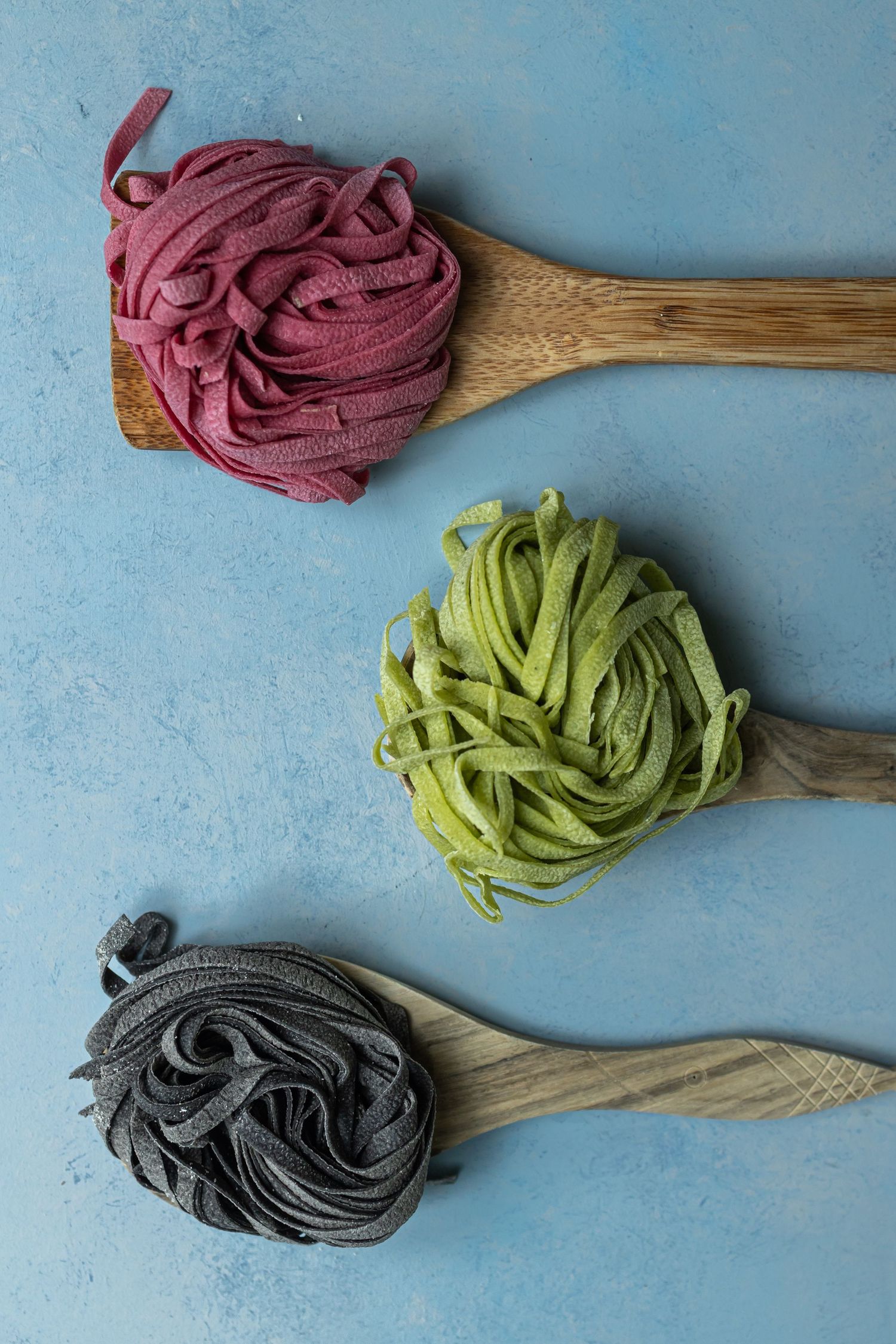 three colours of pasta displayed on wooden spoons in a blue background