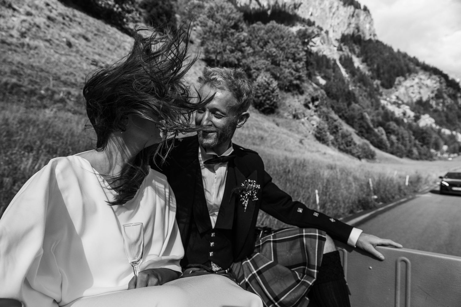 Couple ride in open top landcover, brides hair blows in the wind