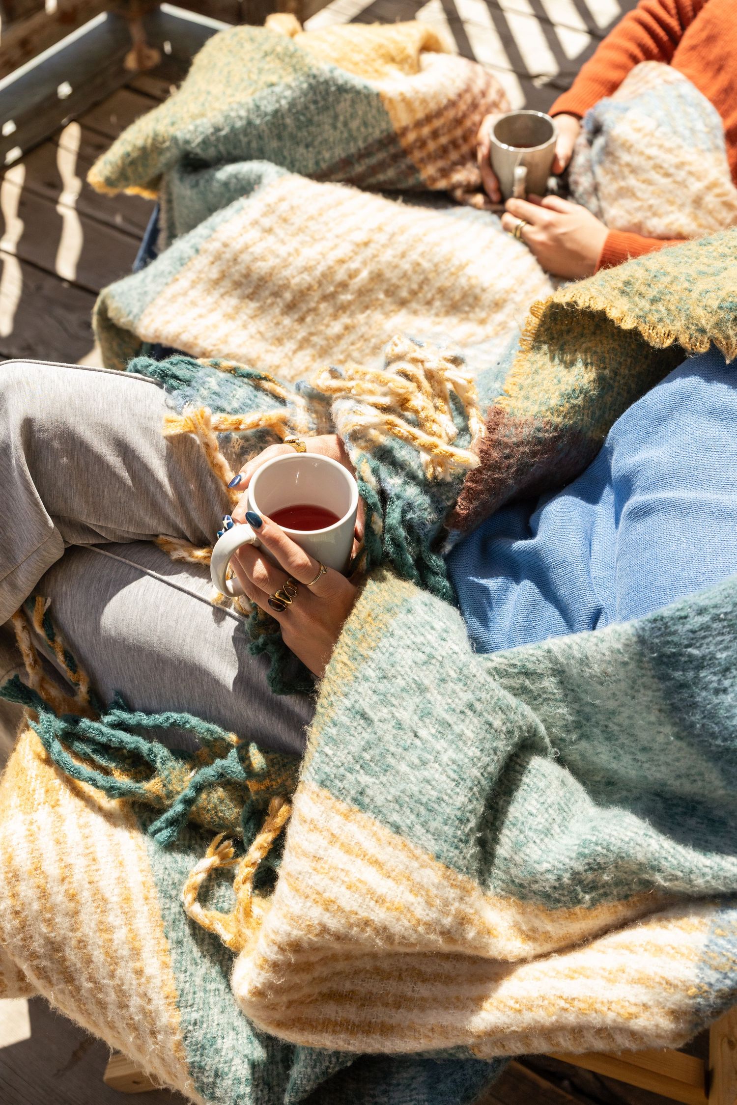 two people sit on balcony with blankets and cups of coffee