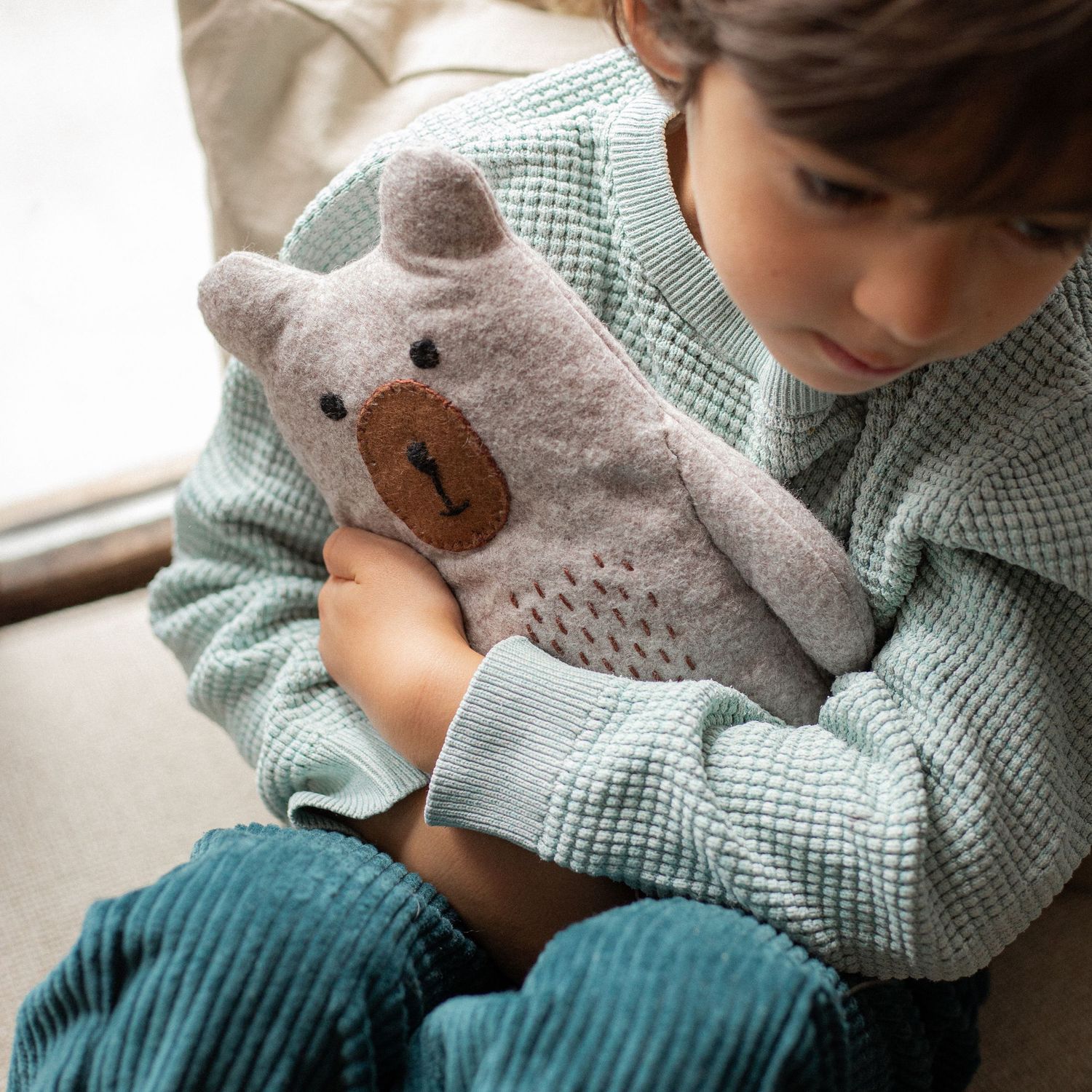 young child in blue cuddling handmade felt teddy in window seat