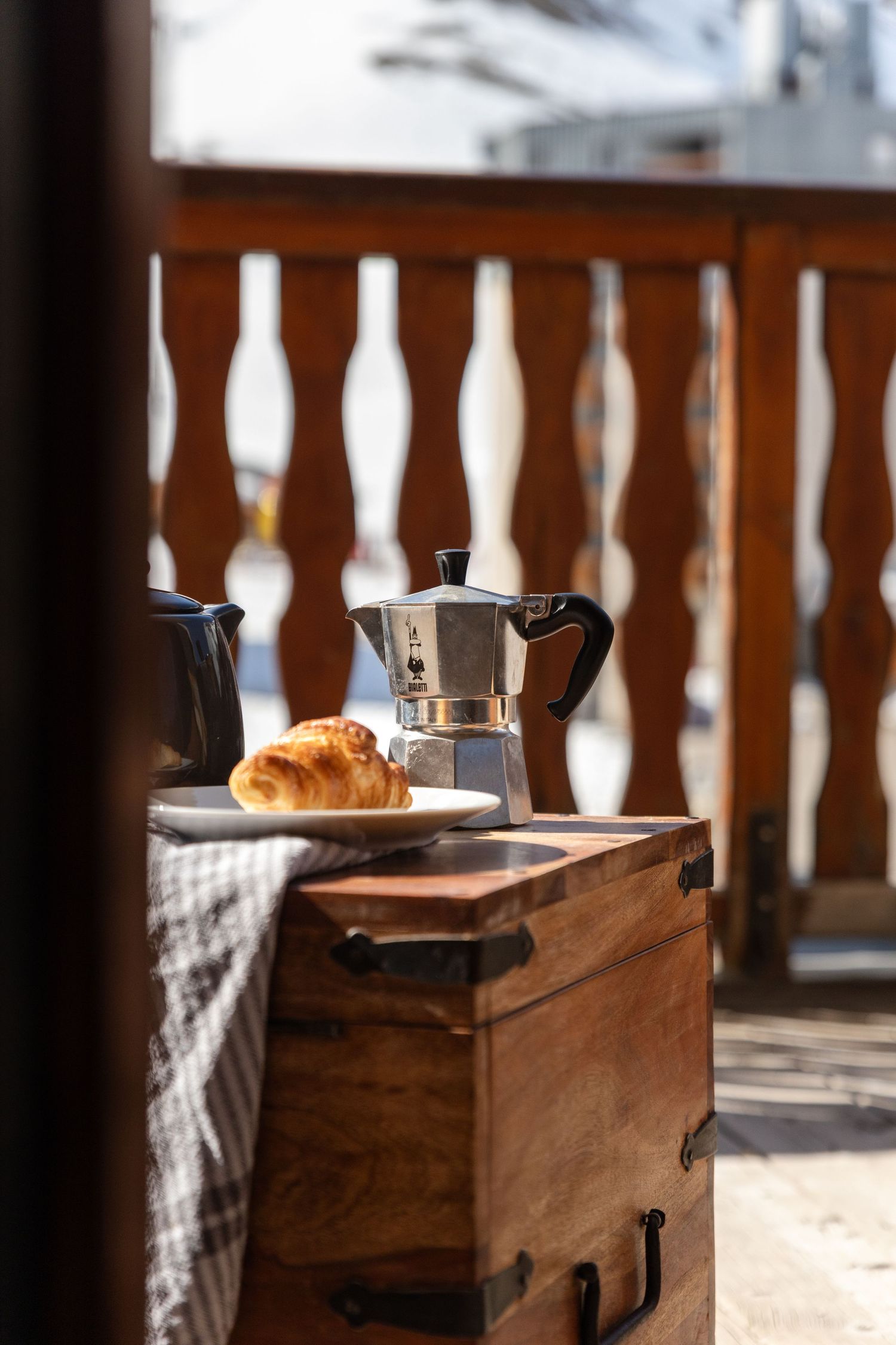 mocha pot and croissant on table on balcony next to ski run