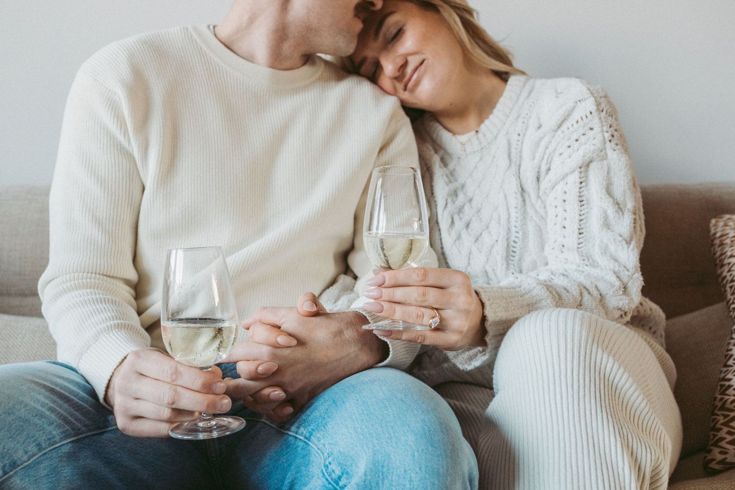 newly engaged couple snuggle on sofa holding hands with glass of champagne