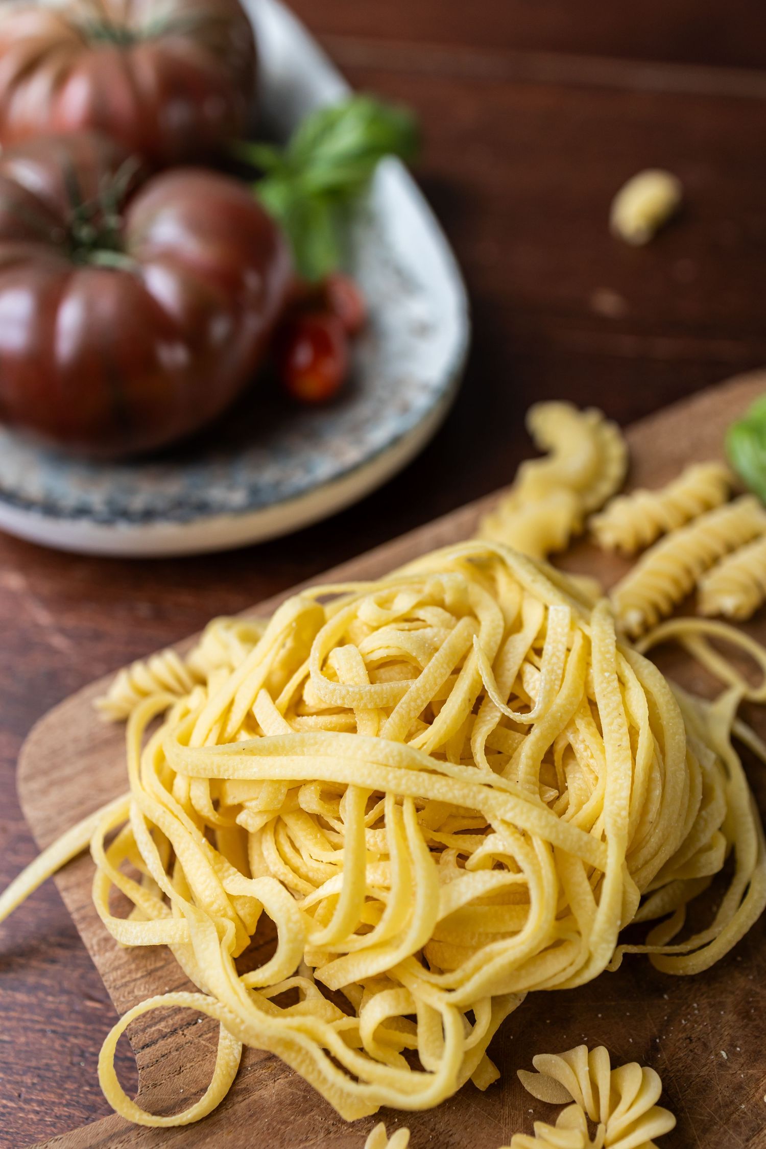 fresh pasta piled in front of dark red tomatoes