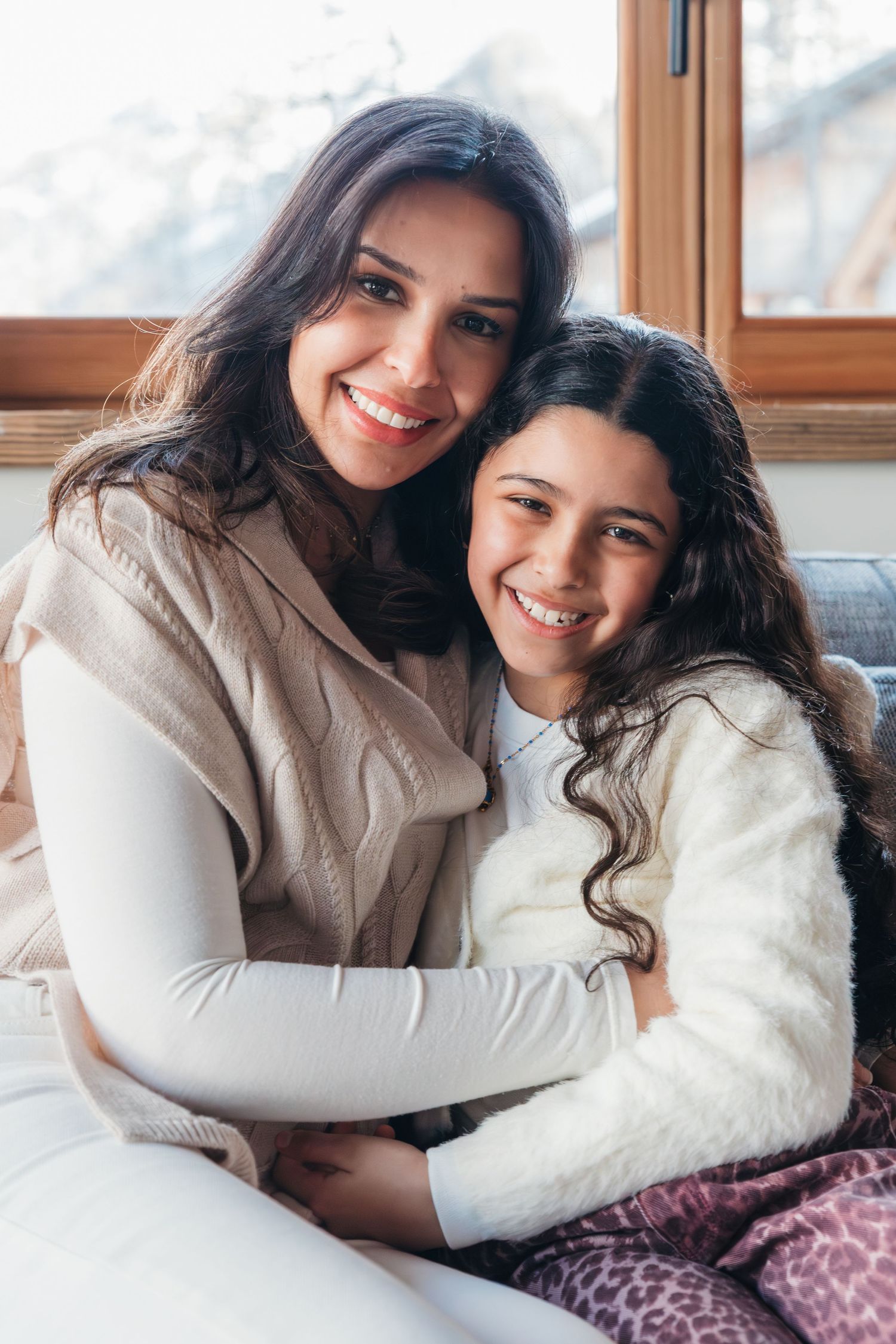 mother and daughter embrace sitting on sofa of their ski chalet
