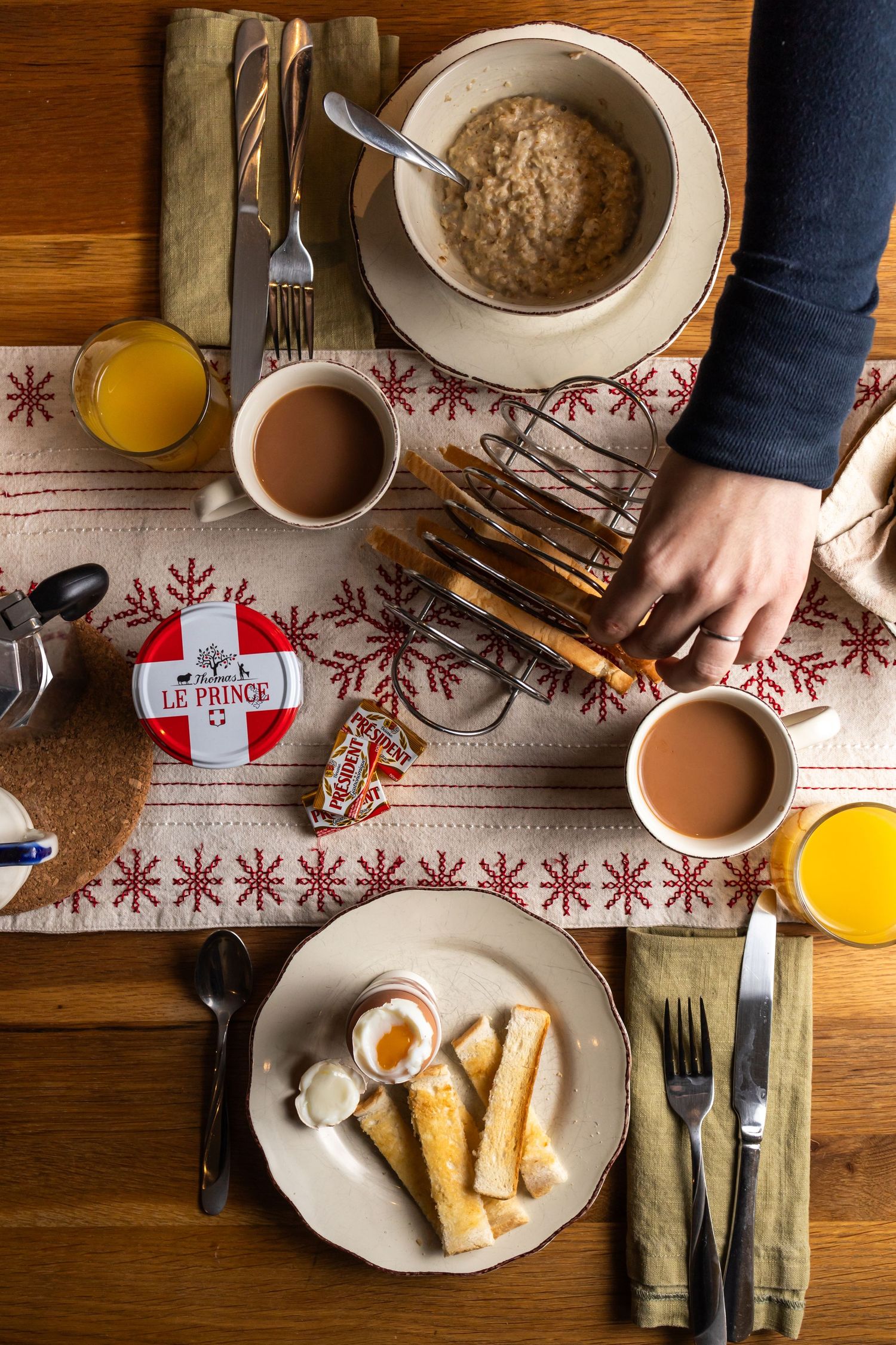 hand reaching across table to take piece of toast from full laid breakfast table