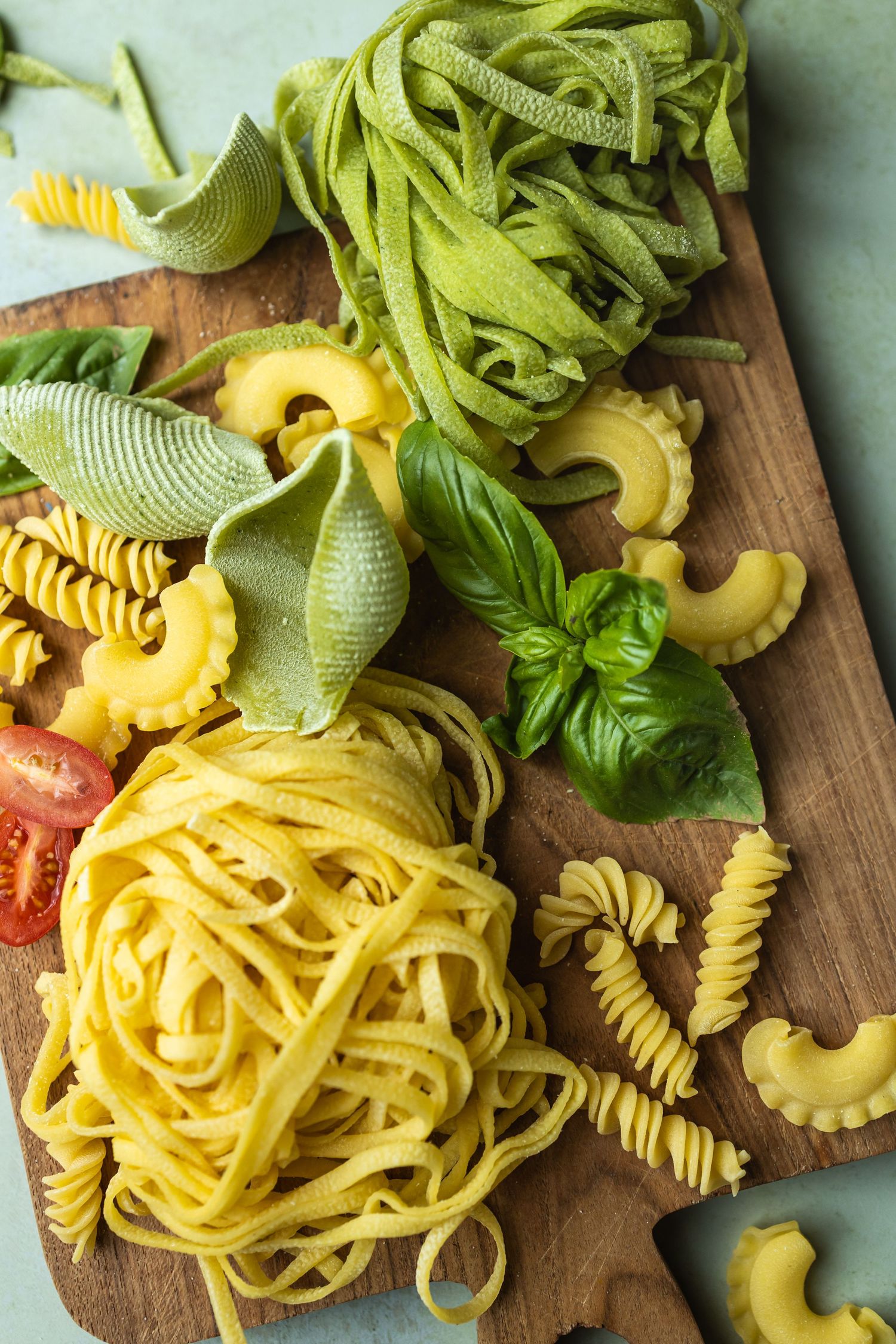 chopping board with fresh uncooked pasta, basil and tomatoes