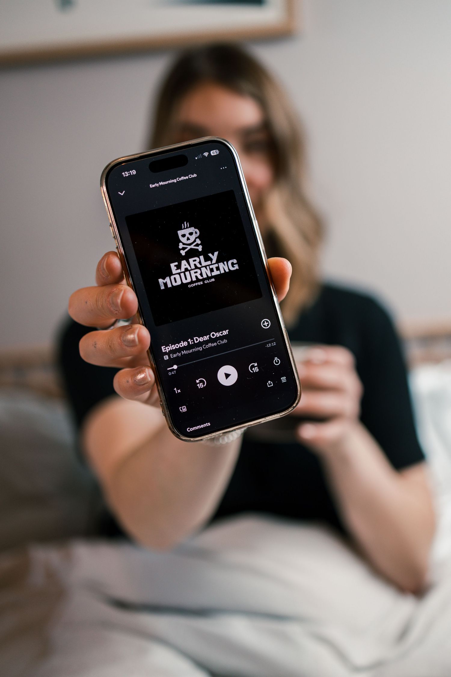female podcaster holding phone up with podcast playing