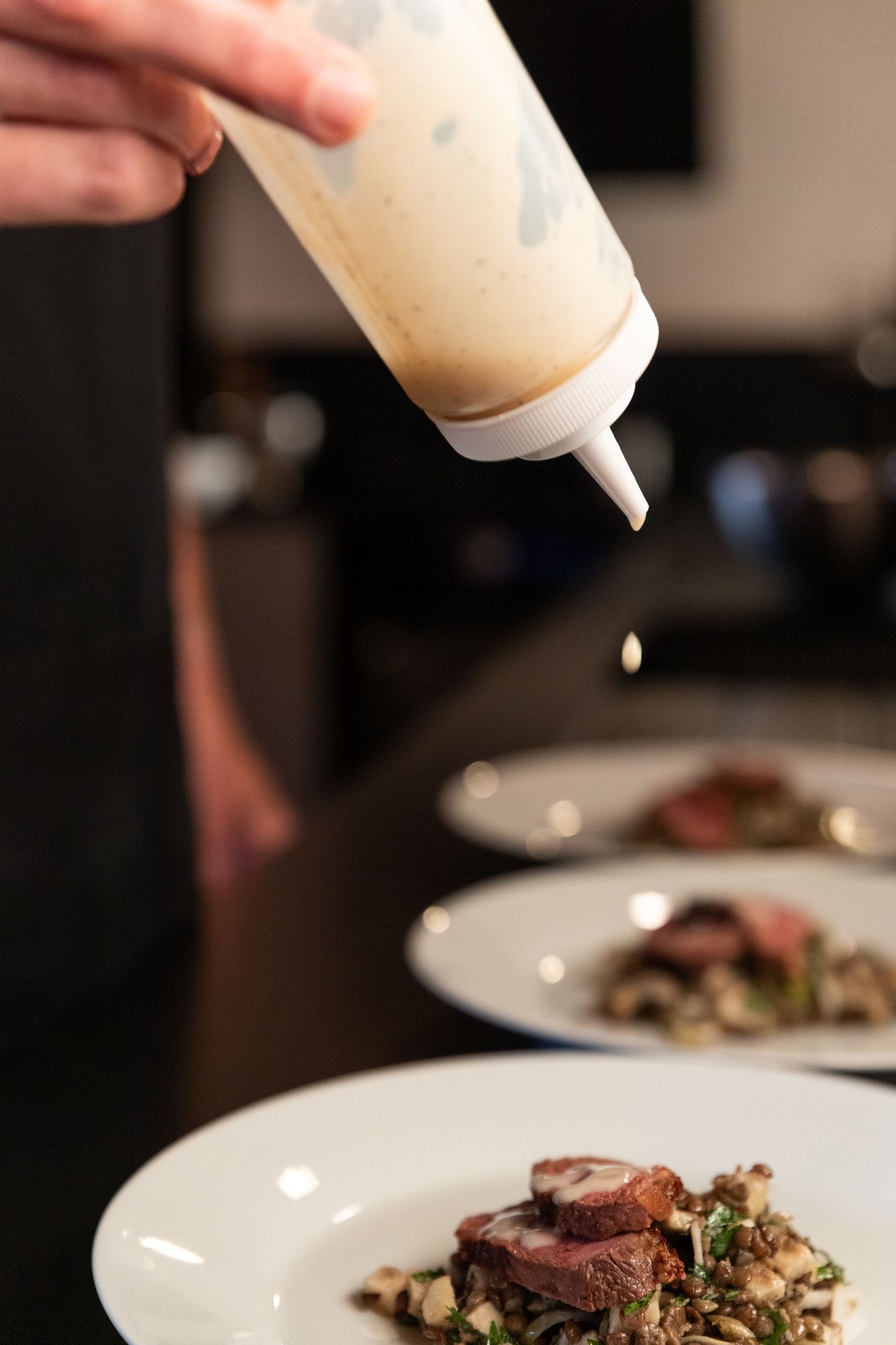 chef adds white liquid to plates using a bottle