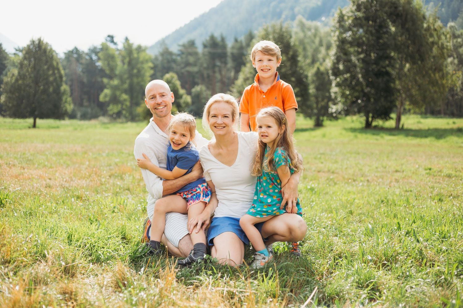 family of 5 pose for photo in field with trees and mountain