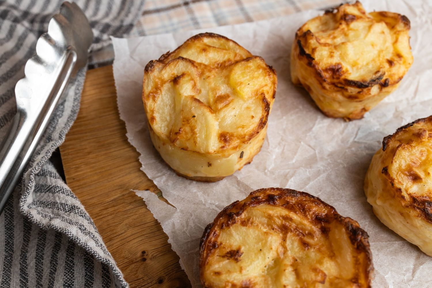 4 individual dauphinoise potato servings on a wooden board next to tongs