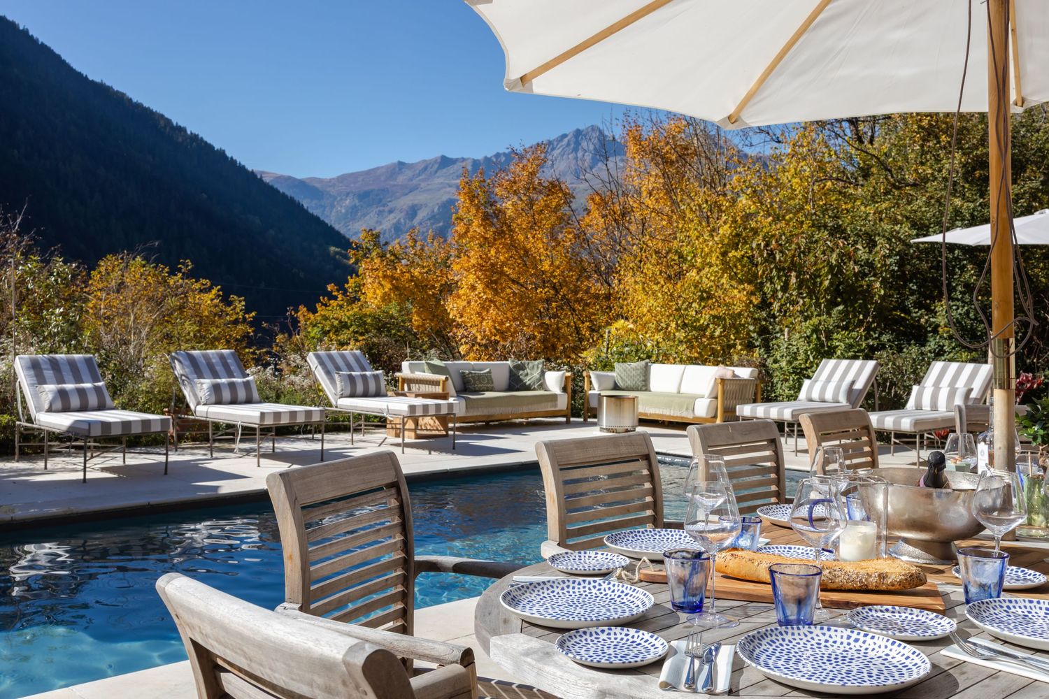 alfresco dining table laid up with blue table wear in front of inviting swimming pool