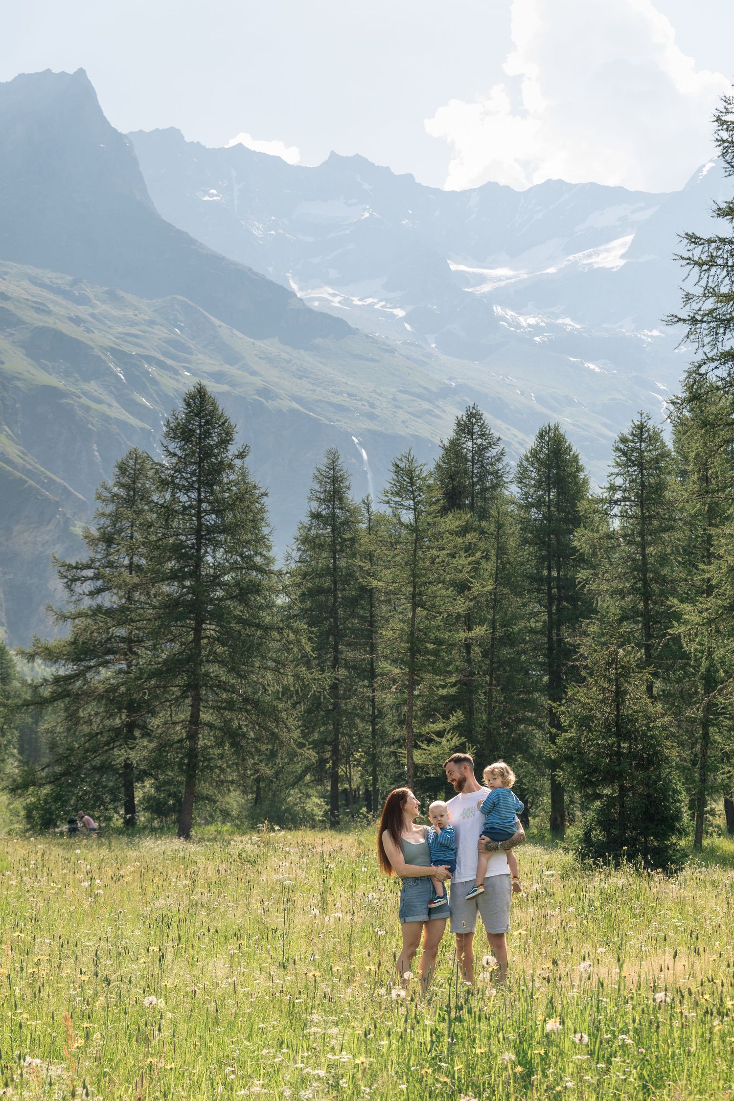 family of four look at each other in field surrounded by large mountains