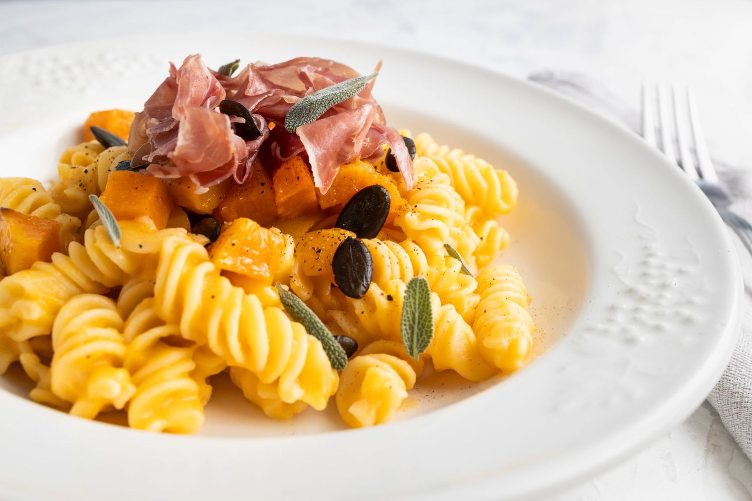 white plate with fresh pasta, dressed with parma ham and seeds