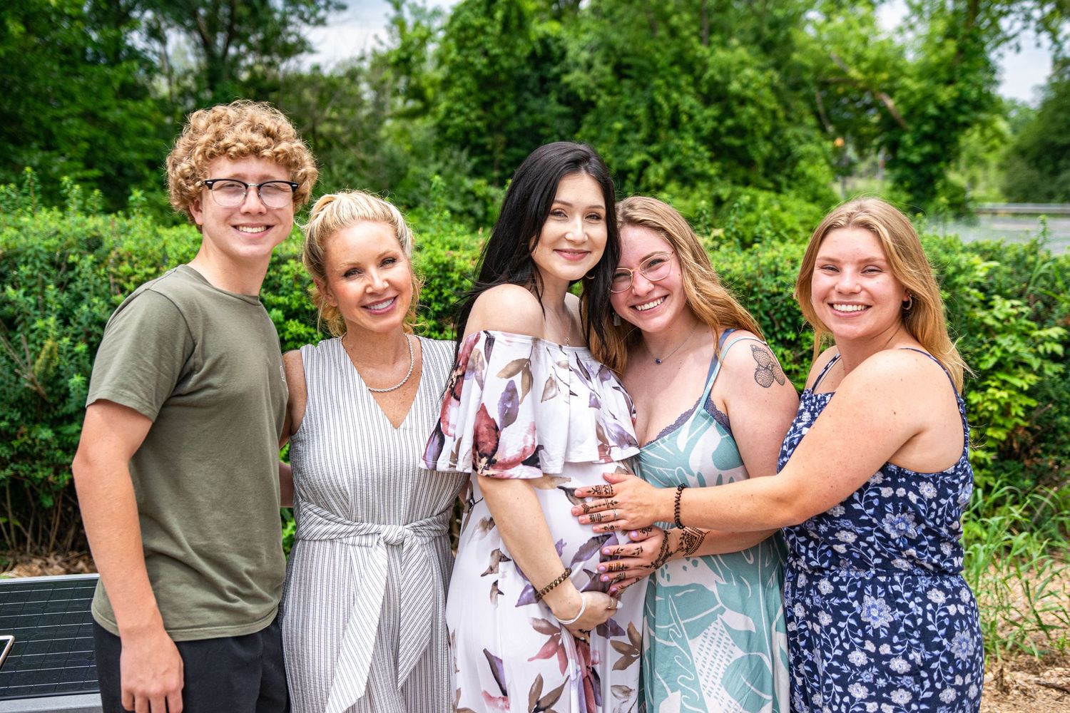 Family portrait session in a lush green outdoor setting on a sunny summer day.