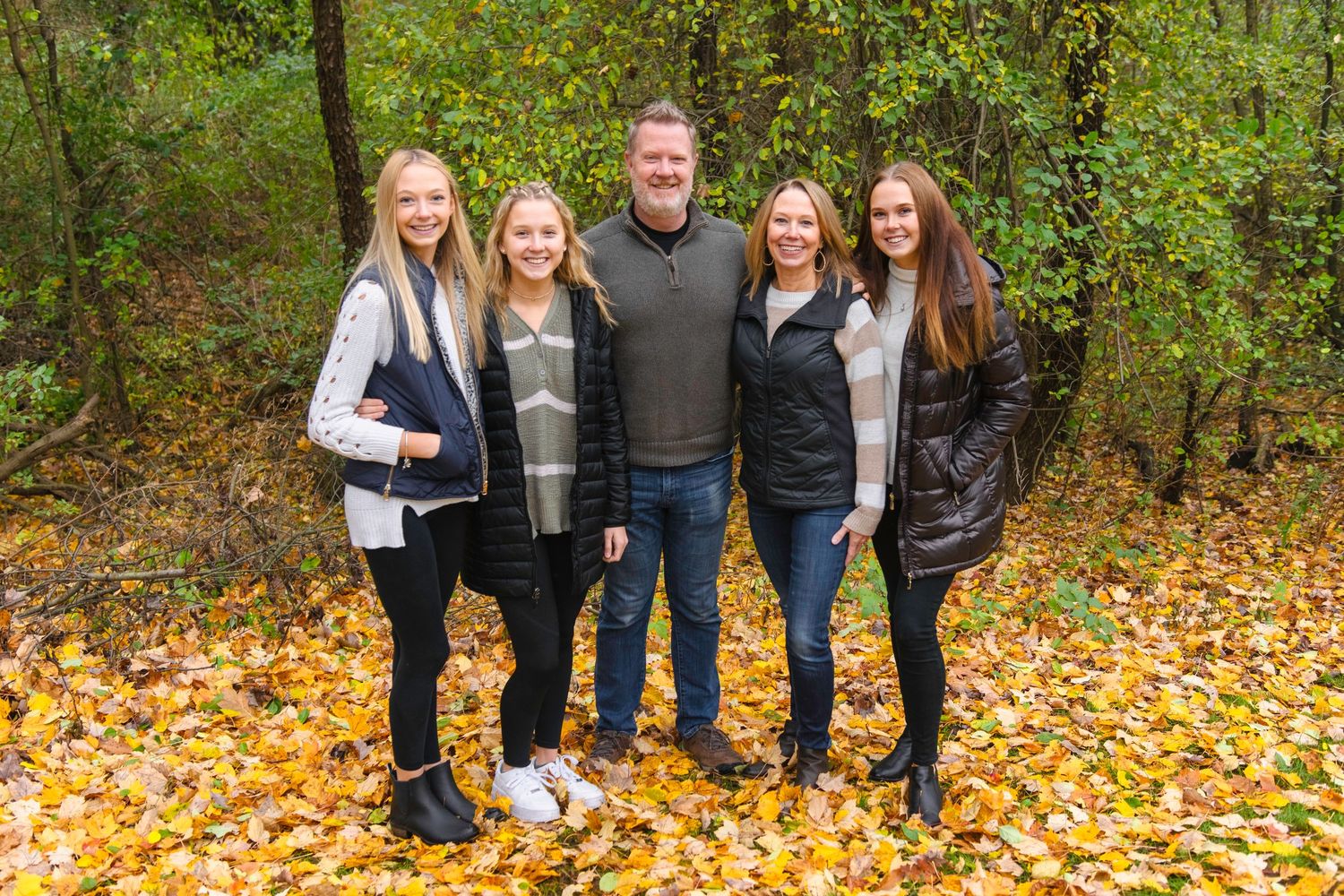 Family group photo on fallen autumn leaves in wooded setting.