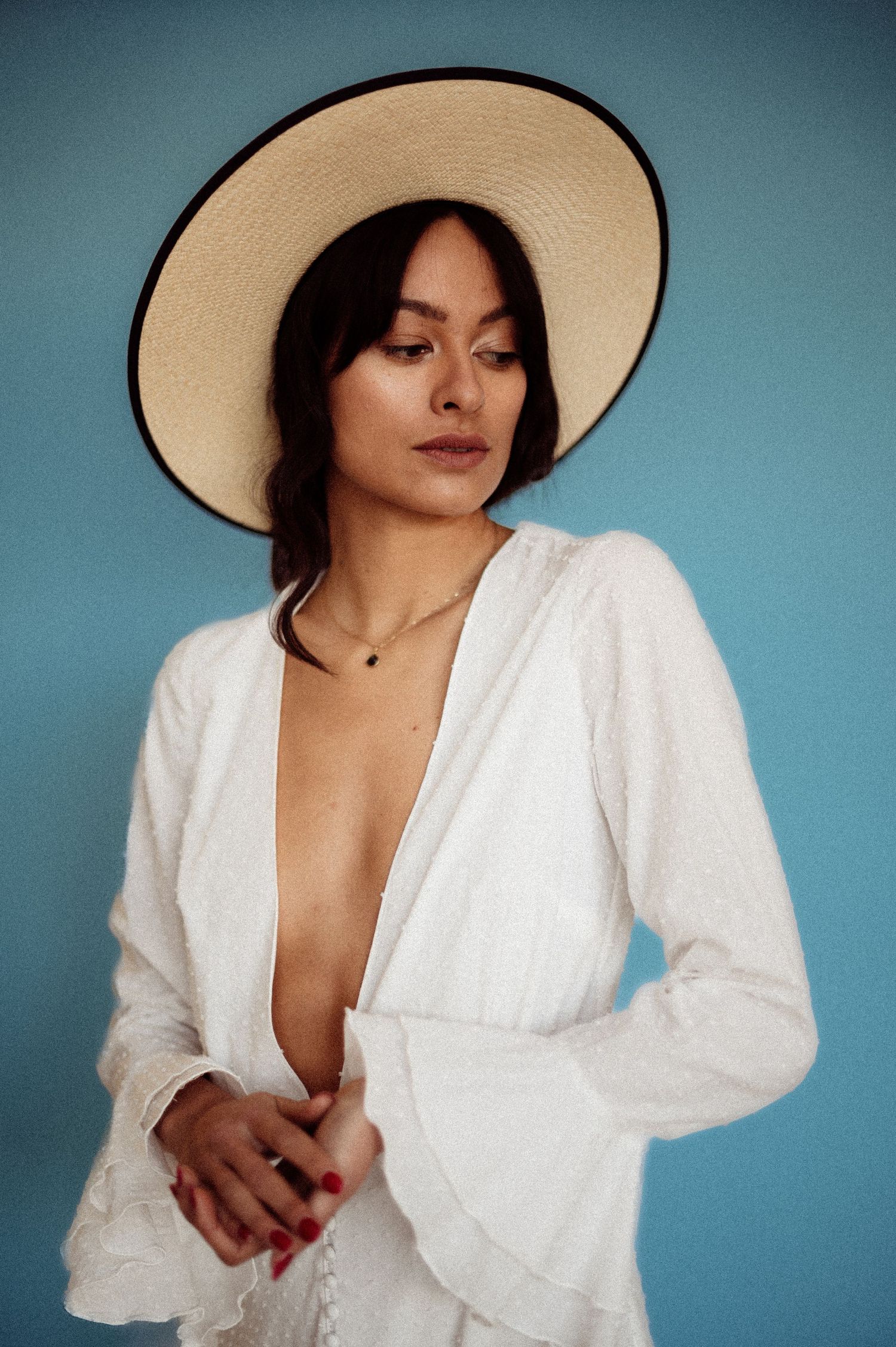 Fashion portrait of a model wearing a white outfit and wide-brimmed hat against a blue background.