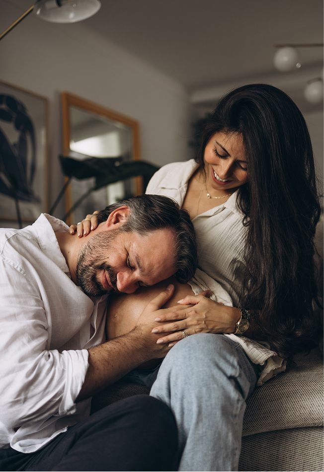 A couple sharing a tender moment on a couch, woman smiling as man rests his head on her lap.