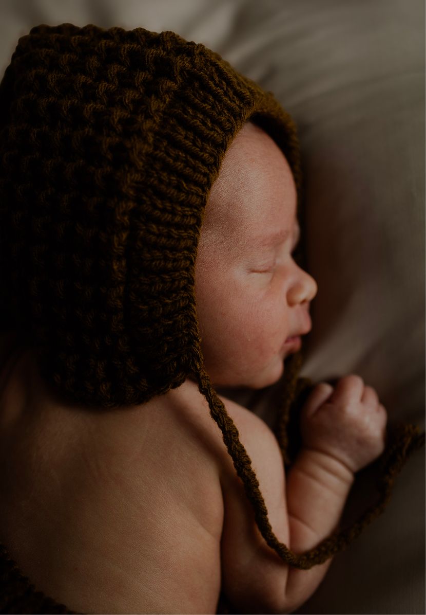 Sleeping newborn baby wearing a brown knitted bonnet in a cozy portrait photo.
