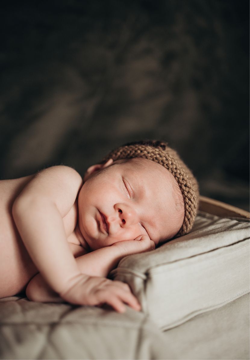 Peaceful newborn baby sleeping on a soft pillow wearing a brown knit hat in a professional portrait.