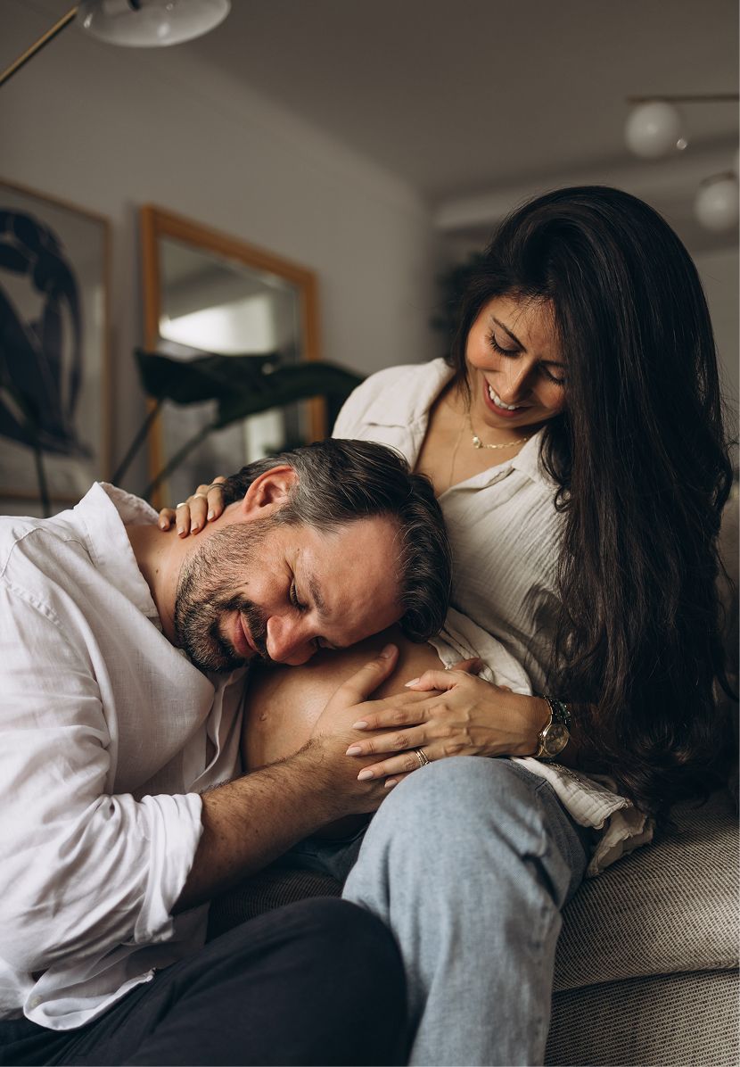 A couple relaxing on a sofa, man resting his head on woman's lap while she smiles warmly at him.