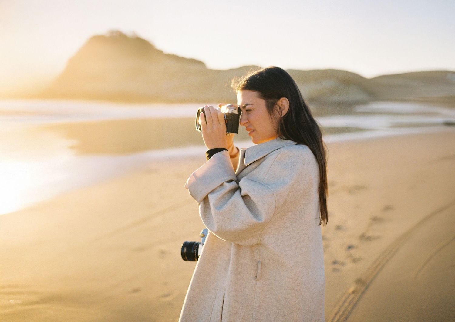 Professional photographer with telephoto lens silhouetted against scenic beach sunset.