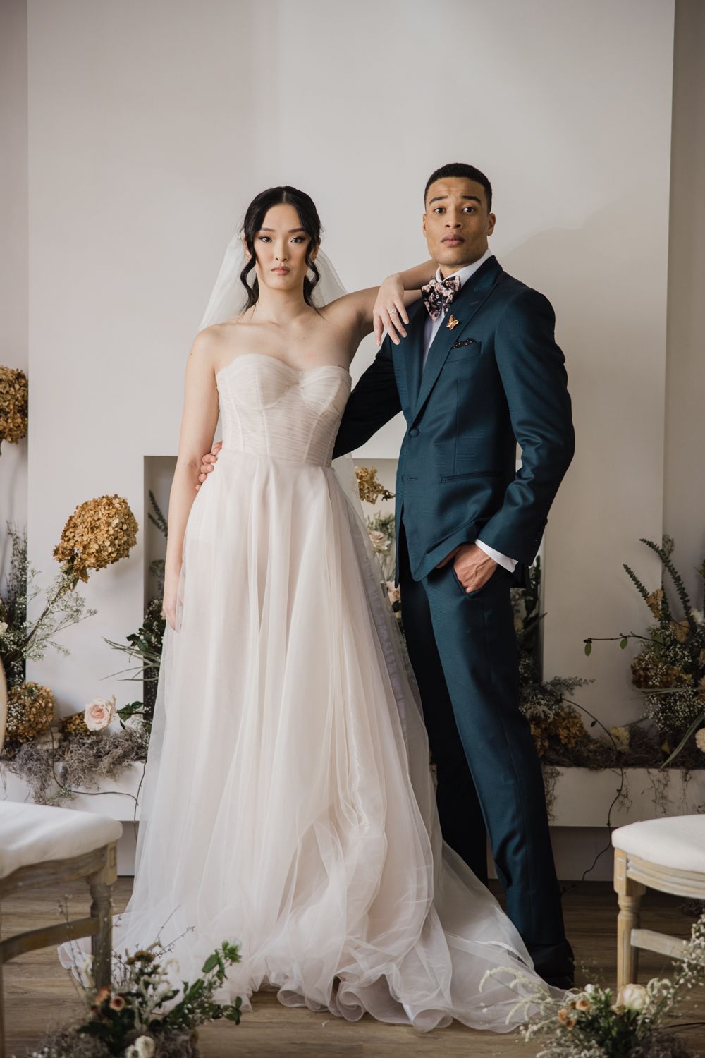 Bride and groom posing together in a stylish setting, with floral decorations enhancing the scene. Professional work of 