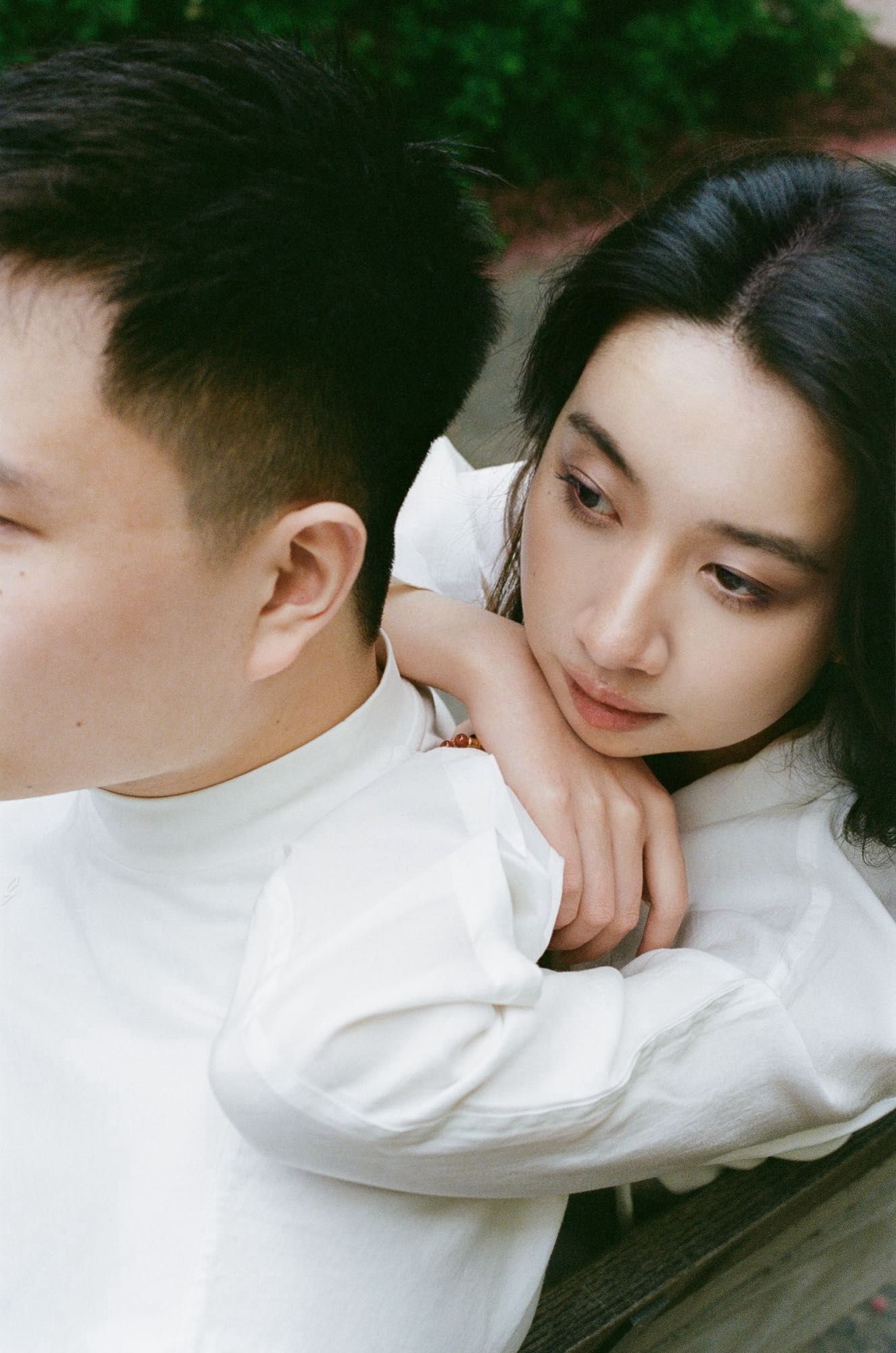 A young couple captured by a film wedding photographer in an intimate moment. The woman leans on the man's shoulder, bot