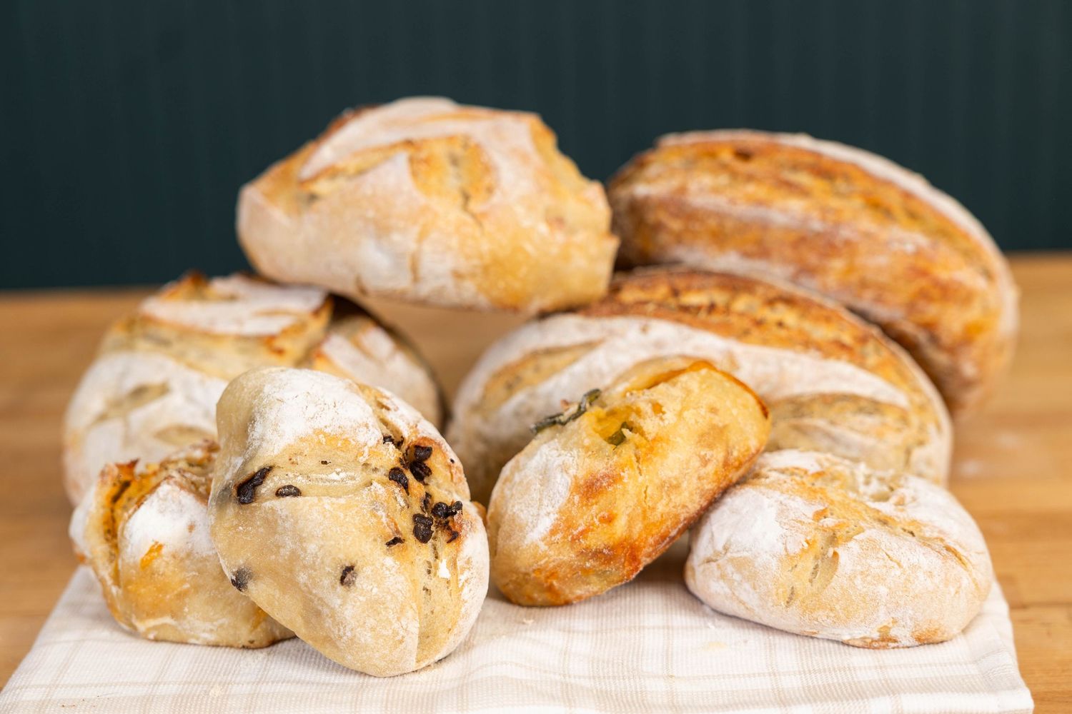 Assorted artisan bread loaves and rolls displayed on a white cloth, showcasing rustic sourdough and olive bread varieties.