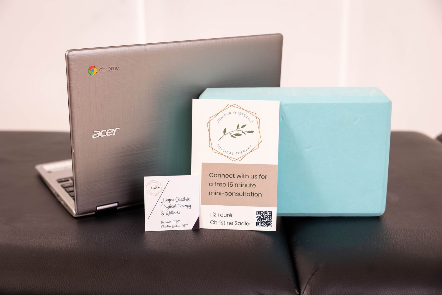 Acer Chromebook laptop beside a teal yoga block and business card on a dark couch for a wellness consultation.