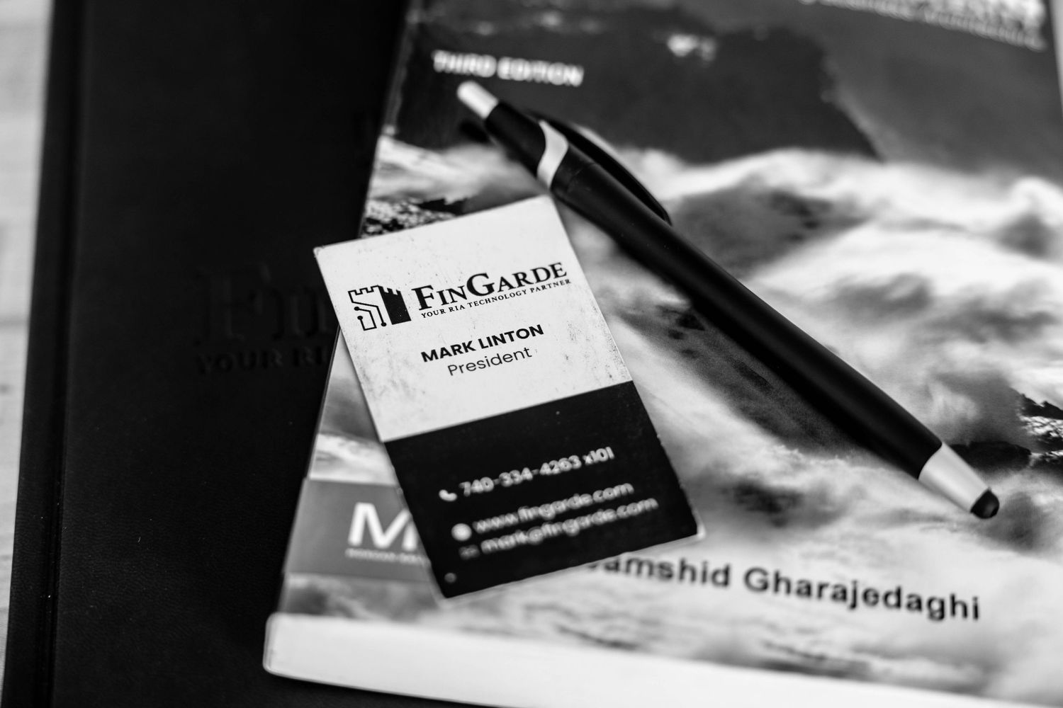 Black and white photo of FinGarde business card for Mark Linton, President, resting on a book with a pen nearby.