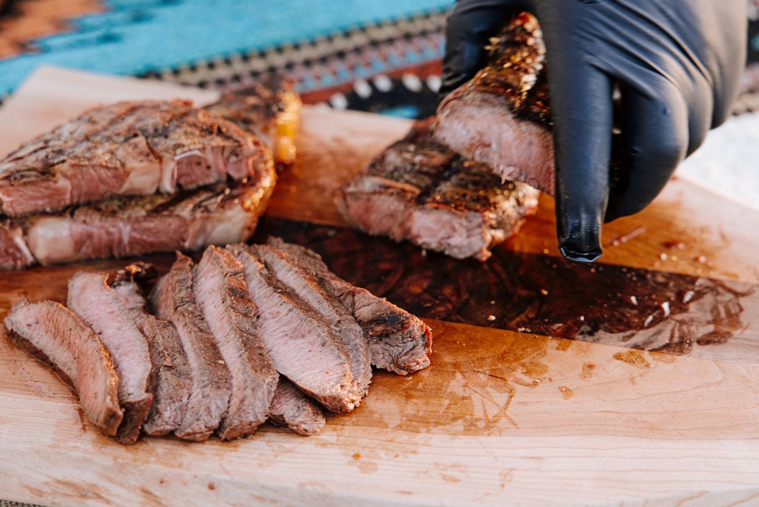 Gloved hand slicing smoked brisket on wooden cutting board with rich juices flowing.