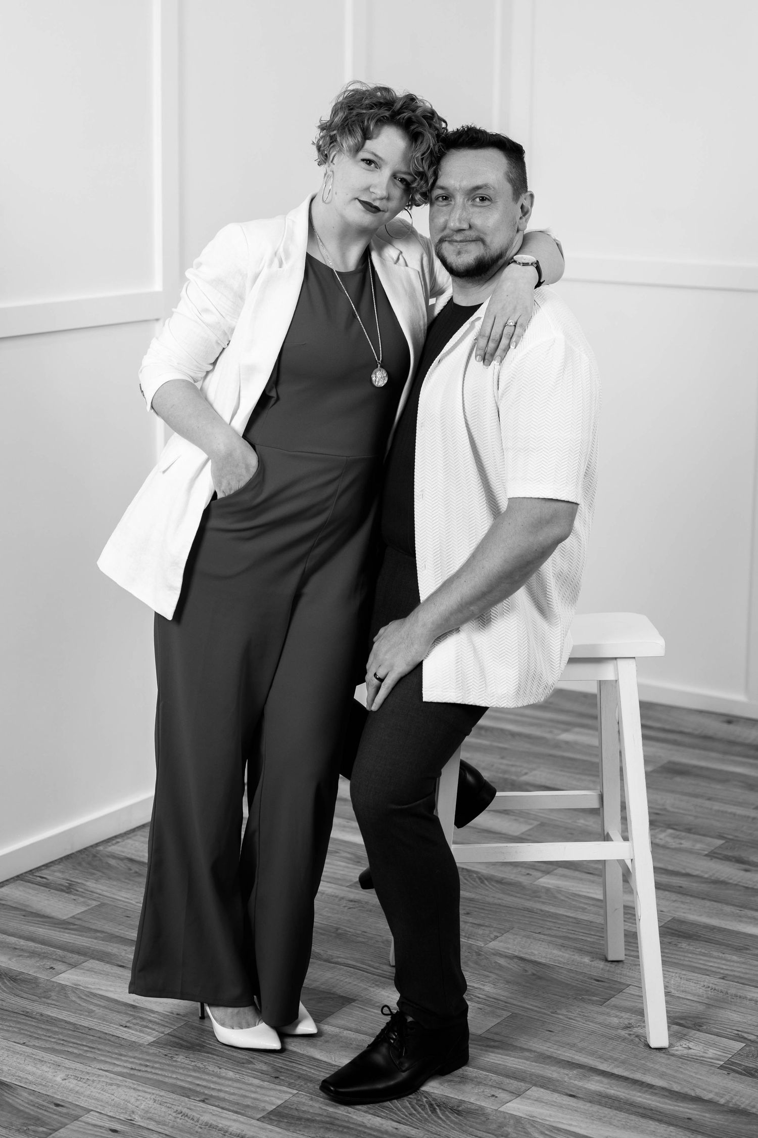 Black and white portrait of a stylish couple posing together in a bright studio, woman in jumpsuit and man in casual shirt.