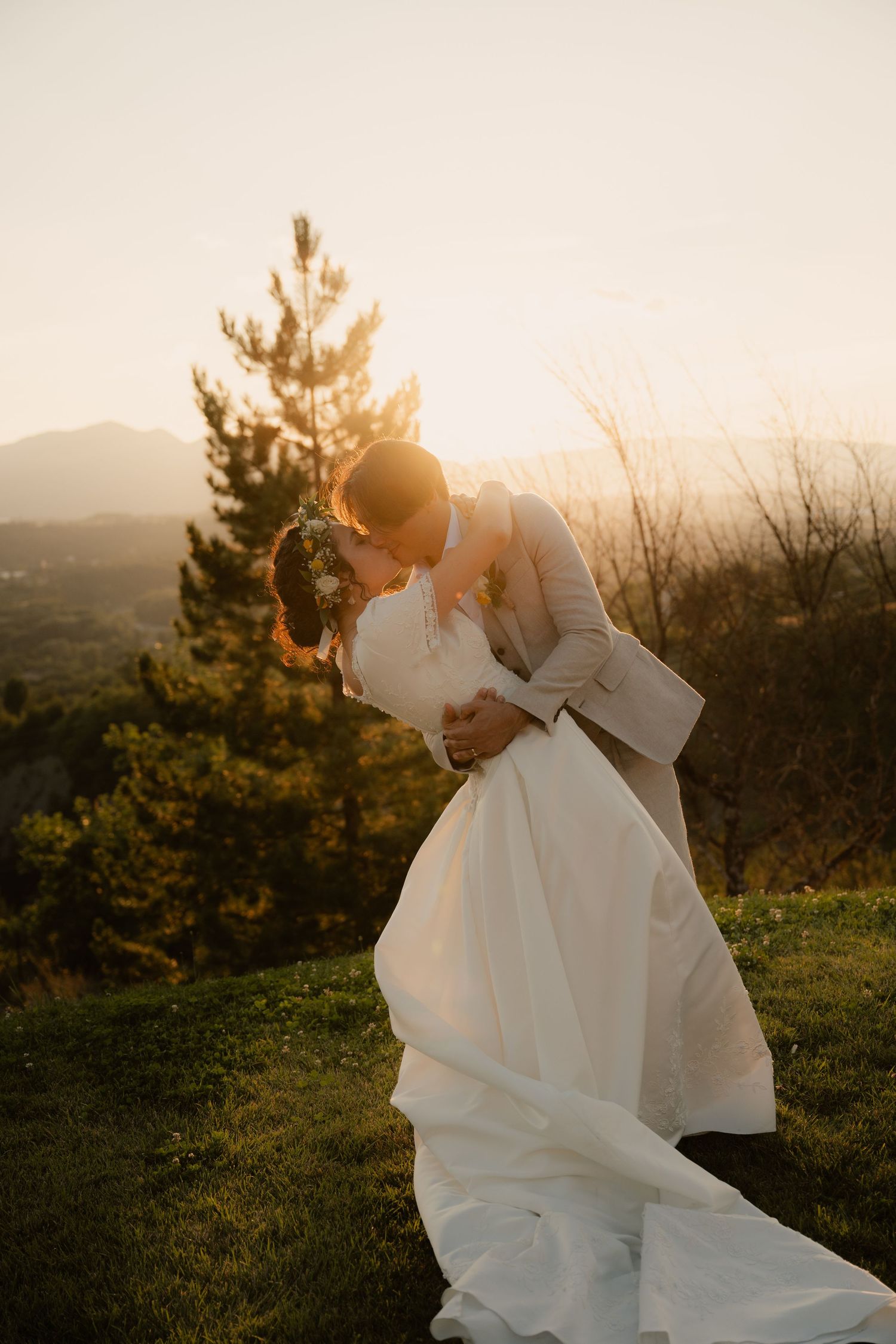 Un moment romantique de mariage au coucher du soleil, immortalisé au sommet d'une colline, avec une robe blanche fluide et une lumière dorée