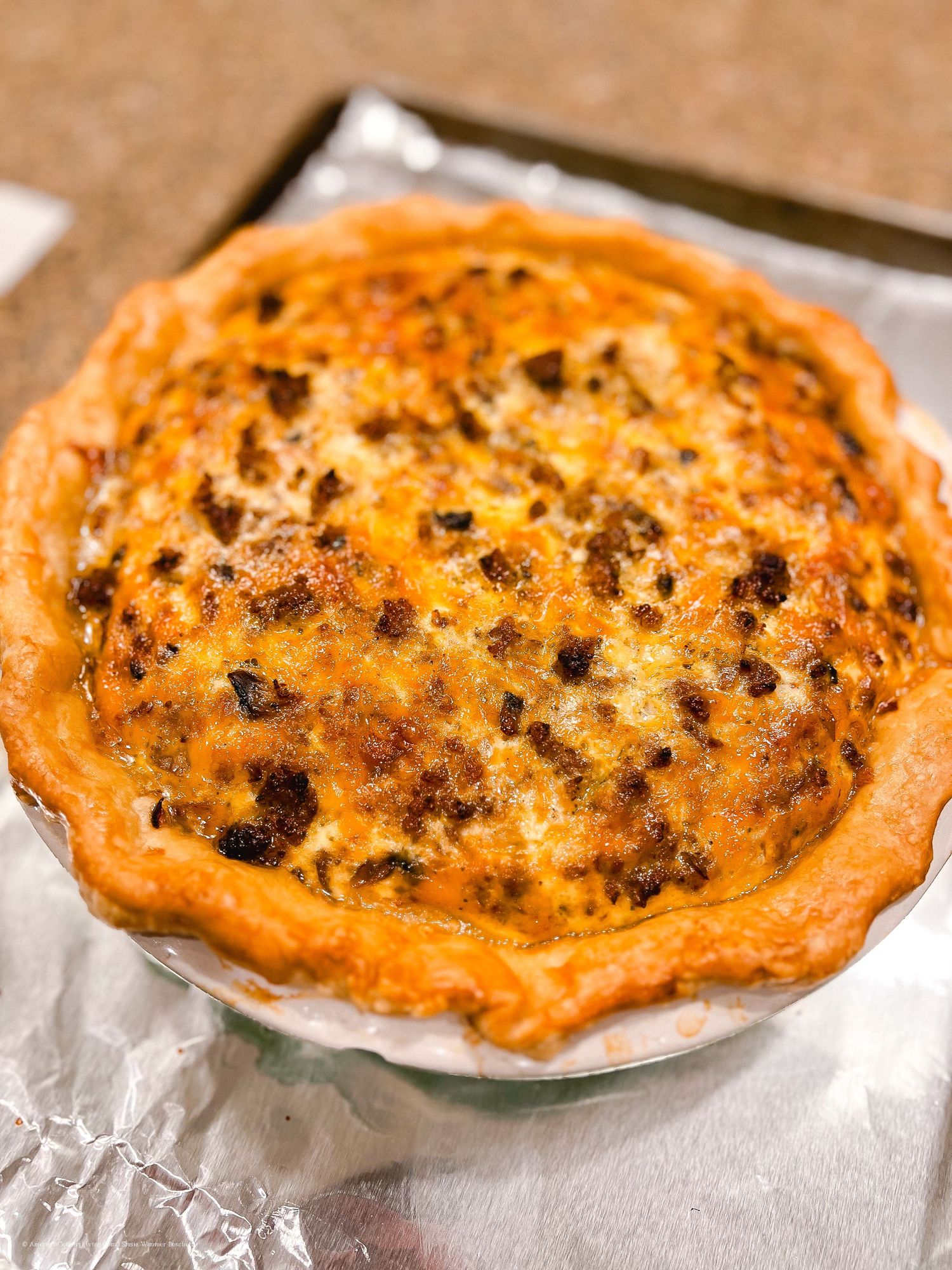 Golden brown pies with melted cheese and meat toppings baked on aluminum foil.