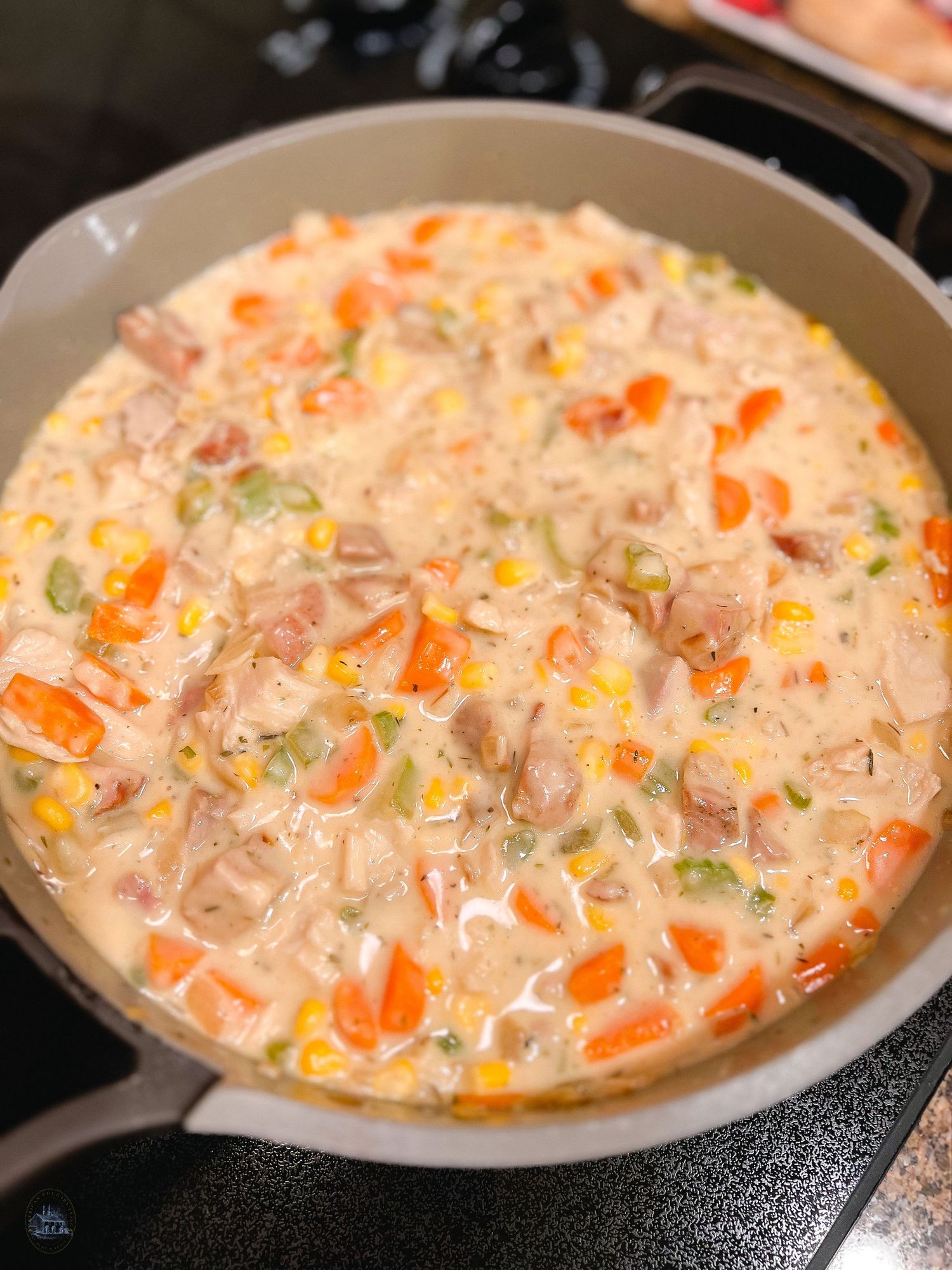 Creamy chicken soup with vegetables simmering in a large pan on stovetop.