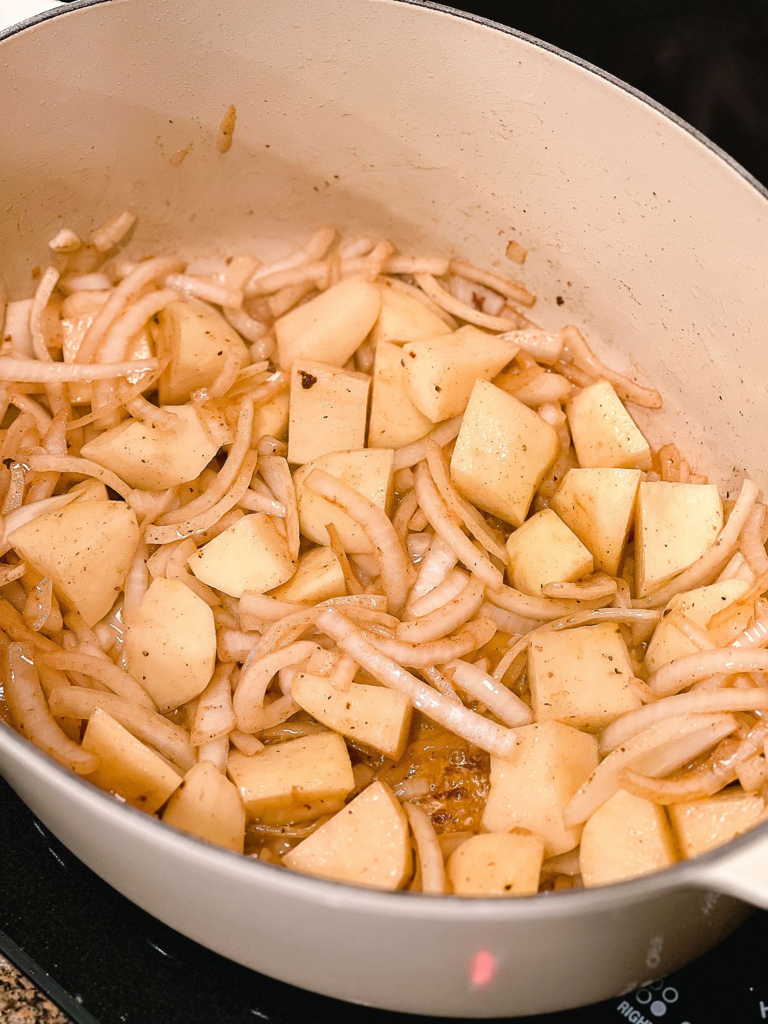 Sliced onions and potatoes cooking in a large white dutch oven.