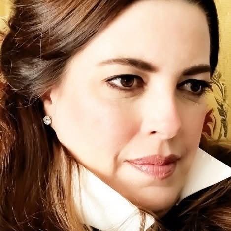 Close-up portrait shot with warm lighting showing long brown hair and pearl earrings.