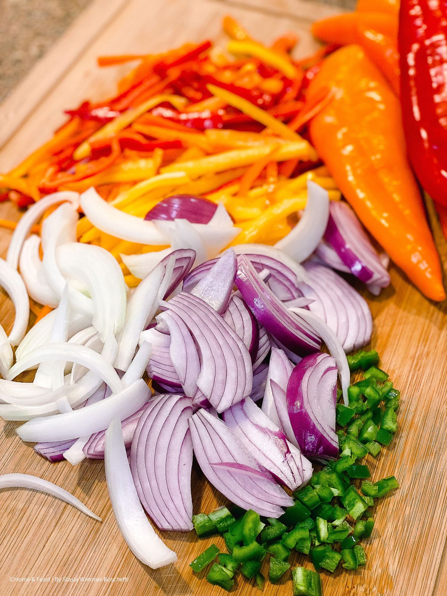 Fresh chopped vegetables including purple onions, orange peppers, and green jalapeños on wooden cutting board.
