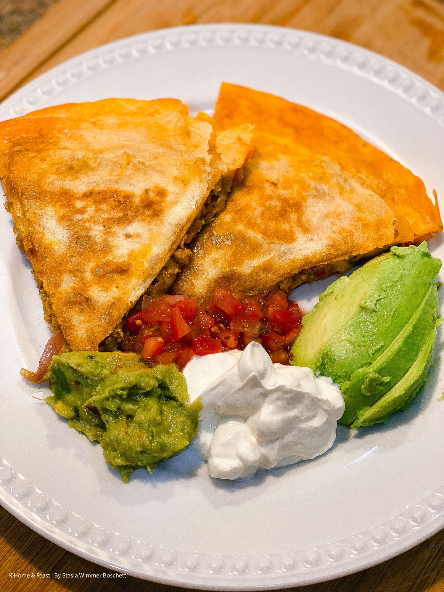 Grilled quesadilla served with fresh avocado slices and sour cream on white plate.