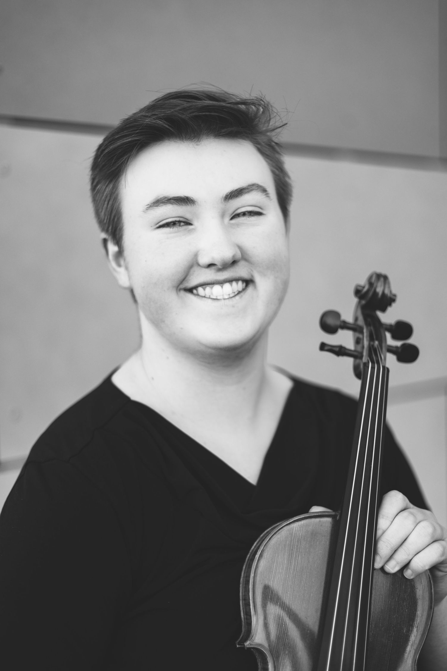 A person with short hair smiles while holding a violin in a black-and-white photo, capturing the essence of musician headshots.